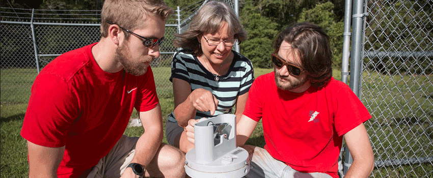 Two Meteorology Students working with professor outside with weather equipment.