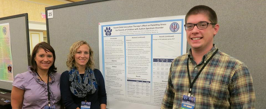 One male and two females standing in front of a presentation hanging on a wall.