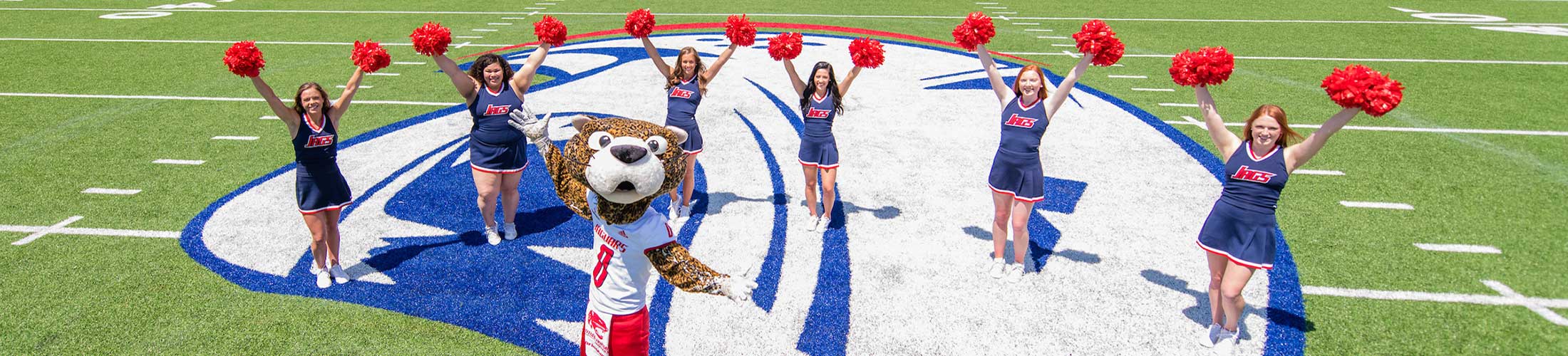 Southpaw on football field with cheerleaders behind him.