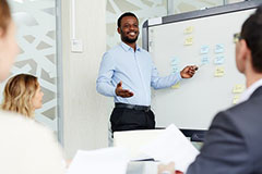 Man speaking at whiteboard smiling with people lookng on.