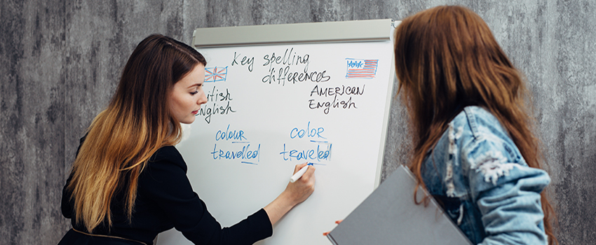 Woman writing on white board while another woman looks on,.