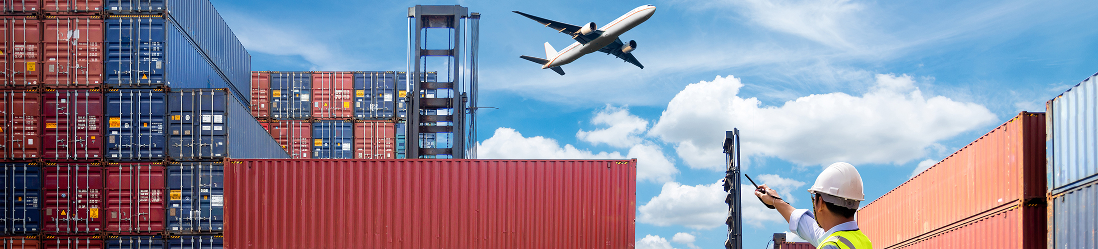 Pane flying over shipping containers with man pointing to the sky in hard hat.