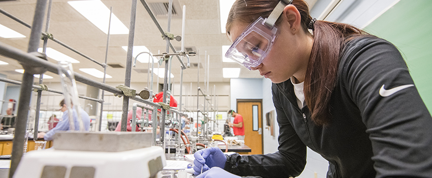 Student working in lab with safety glasses on looking at specimen.