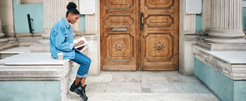 Student looking at book sitting on edge of building.