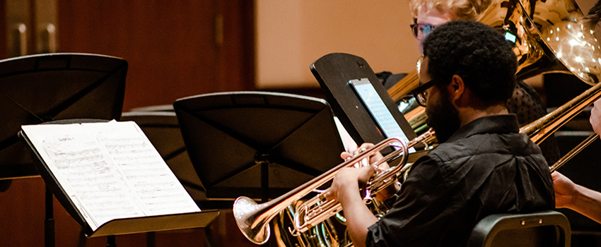 Music student playing trumpet looking at music.