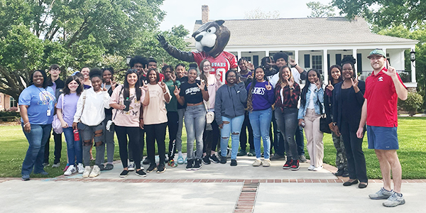 A group of students standing in front of Southpaw statue holding up the J sign for Jaguars.