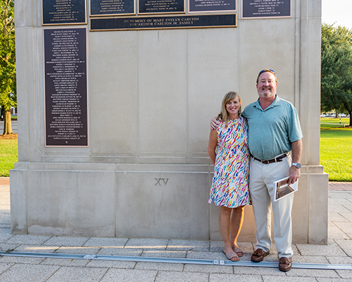 Two alumni in front of the Wall of Honor on campus.