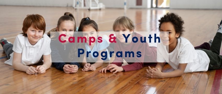Children in a gym setting on the floor looking and smiling at a camera