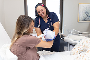 USA Health nurse handing baby to mother in hospitall room.