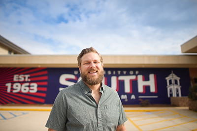 Adult Learner student standing in front of South mural.