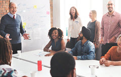 Man speaking to group around table in front of white board